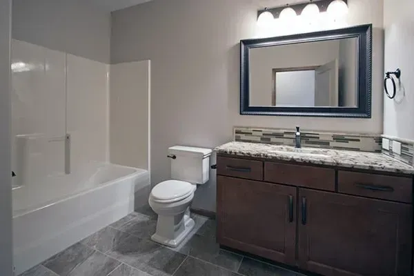 Small modern bathroom with a tub, toilet, dark vanity, and large mirror
