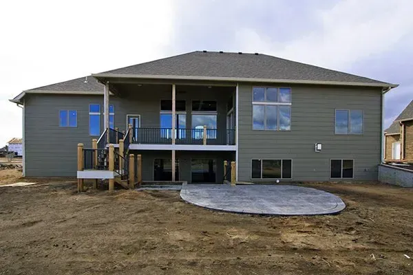 New gray house under construction with a raised back deck and bare dirt yard