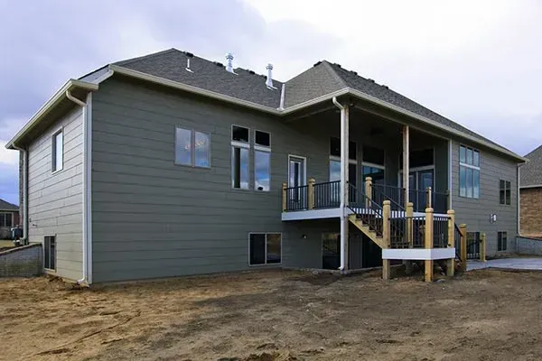 New gray house with a covered deck and stairs on a dirt lot