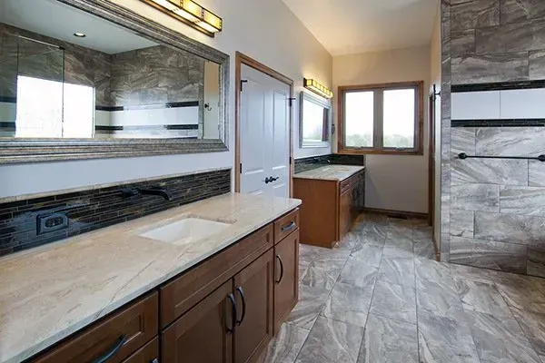 Modern bathroom with marble vanity, large mirror, tub, window, and gray tile flooring