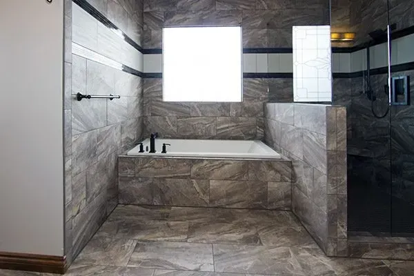 Modern tiled bathroom with a built-in bathtub, walk-in shower, and large window.