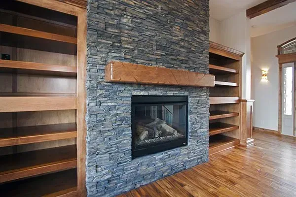 Stone fireplace with wooden mantle, built-in shelves, and hardwood floors in a living room