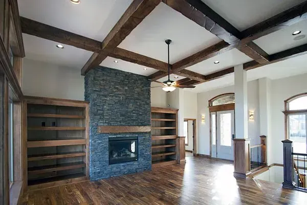 Spacious living room with wood floors, exposed beams, built-in shelves, and a stone fireplace.