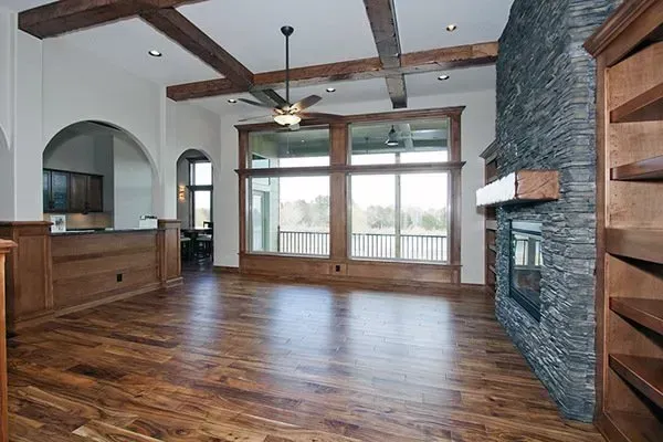 Spacious living room with hardwood floors, stone fireplace, exposed beams, and large windows overlooking a deck