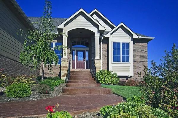 Front view of a brick house with a blue front door, stone steps, and landscaped yard