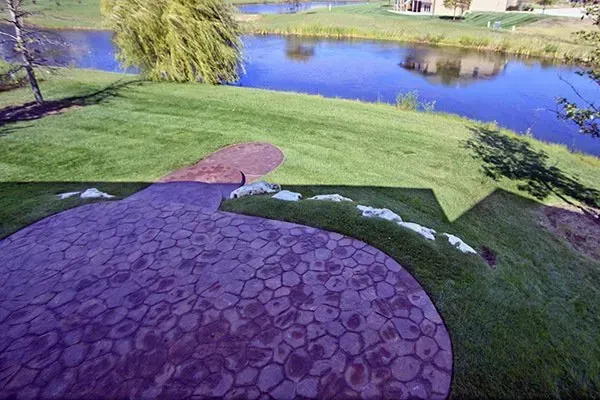 Stone patio with a curved edge beside a grassy lawn and pond on a sunny day