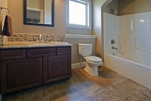 Bathroom with dark wood vanity, toilet, window, and white bathtub/shower.