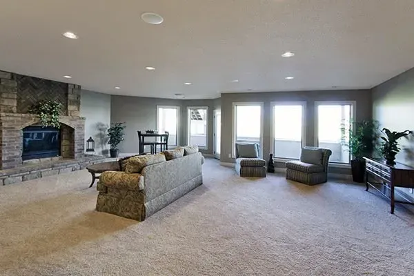 Spacious living room with stone fireplace, sectional sofa, carpet, and bright windows overlooking a patio