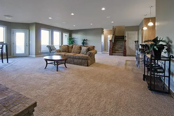 Spacious carpeted living room with sectional sofa, coffee table, staircase, and large windows