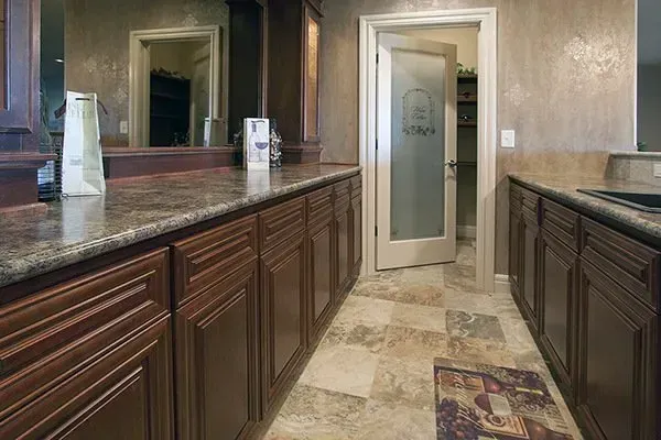 Luxury bathroom with dark wood vanities, granite countertops, beige tile floor, and glass shower door