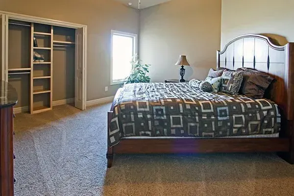 Bedroom with a wooden bed, patterned quilt, and open closet in a carpeted room