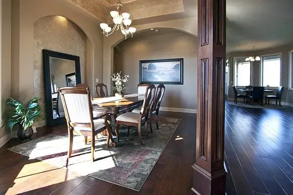 Formal dining room with wooden table, chairs, chandelier, and dark hardwood floors, opening to a living area.