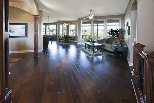 Spacious living room with dark wood floors, large windows, and a glass coffee table.