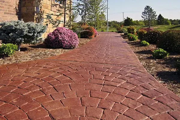 Red brick garden path bordered by shrubs and flowers in a sunny park