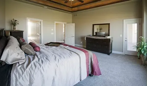 Spacious bedroom with a bed, dresser, white doors, gray carpet, and wood-paneled ceiling.