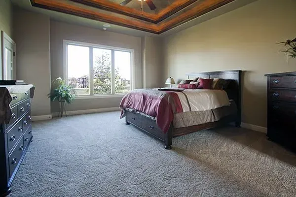 Spacious bedroom with a bed, carpeted floor, dresser, and large window letting in daylight
