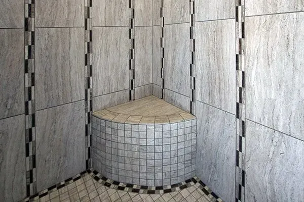 Tiled shower corner with a curved built-in seat and light gray wall and floor tiles