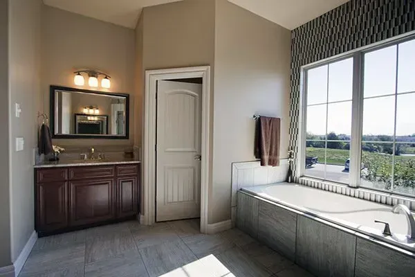 Modern bathroom with dark vanity, large mirror, and soaking tub beside a window overlooking greenery