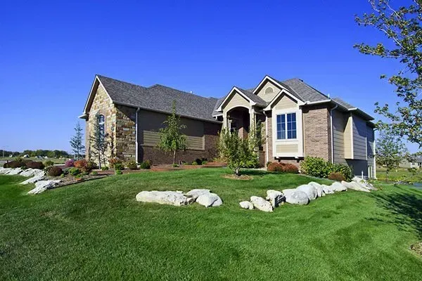 Suburban house with stone and beige siding, green lawn, white rocks, and clear blue sky