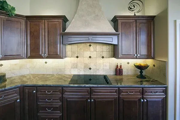 Dark wood kitchen cabinets with green countertop, beige tile backsplash, and stainless range hood