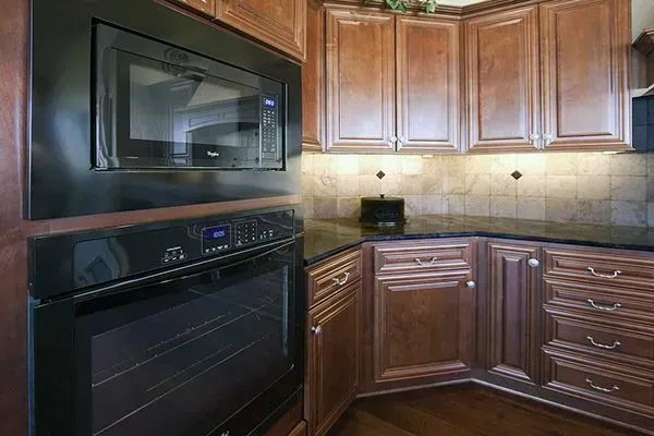 Modern kitchen corner with dark wood cabinets, black built-in oven and microwave, and tan tile backsplash