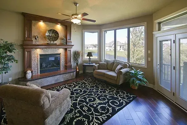 Sunlit living room with fireplace, large windows, sofas, patterned rug, and glass doors