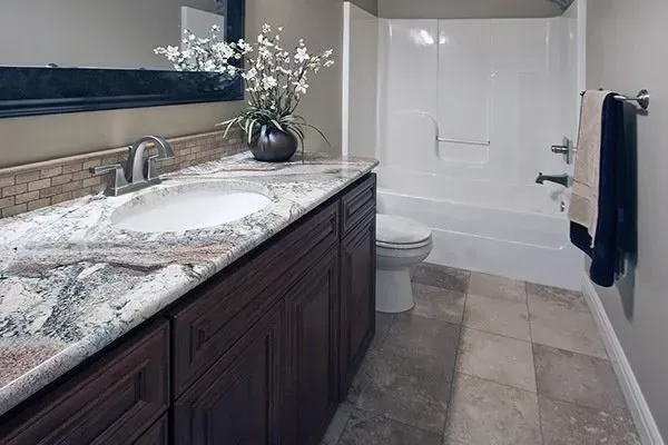 Modern bathroom with marble vanity, sink, toilet, tub, and gray tile floor, accented by dark cabinetry and towels