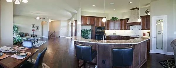 Open-plan kitchen and dining area with wood floors, granite island, and dark cabinets in a bright home