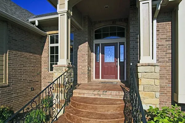 Front entrance of a brick house with red double doors, stone steps, and wrought-iron railings
