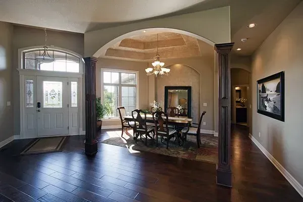 Elegant dining room with arched entry, dark wood floors, chandelier, and table set by large windows