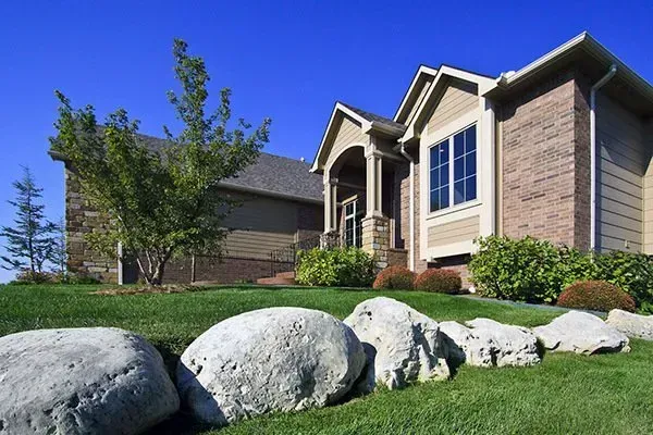 Suburban house with stone siding and large boulders in the front lawn under a clear blue sky
