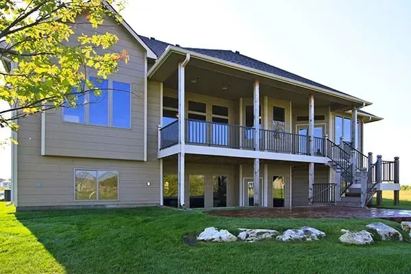 Two-story beige house with a front porch, balcony, and green lawn under a bright sky