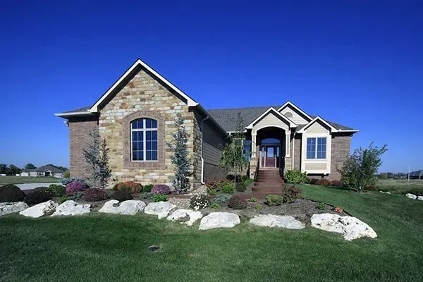 Stone house with arched window and front porch, set in a green lawn under a clear blue sky