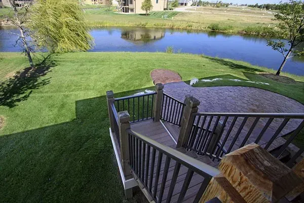 Wooden deck stairs overlooking a green lawn and a pond on a sunny day