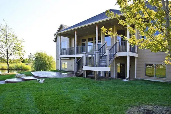 Two-story house with a blue roof, deck stairs, and a grassy backyard under bright sunlight