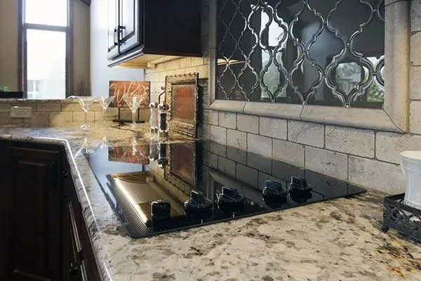 Modern kitchen countertop with stovetop, granite counters, and tiled backsplash near a window