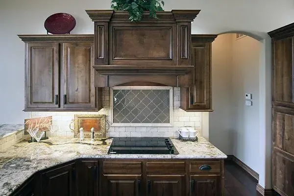 Kitchen with dark wood cabinets, granite countertop, and stainless range under a decorative hood.