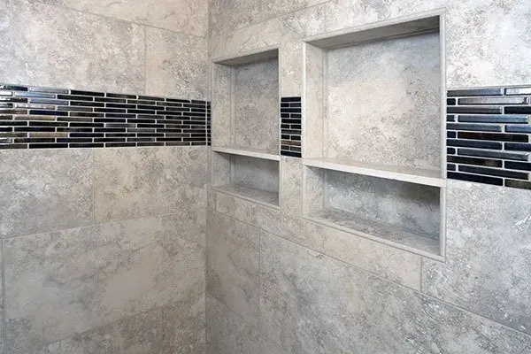 Gray tiled shower with two recessed shelves and black mosaic accent strip along the wall