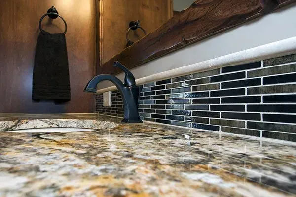 Bathroom sink with black faucet, wood wall, and blue-black mosaic backsplash behind a stone countertop