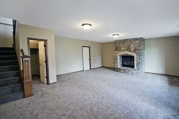 Spacious carpeted living room with a stone fireplace and two ceiling lights.