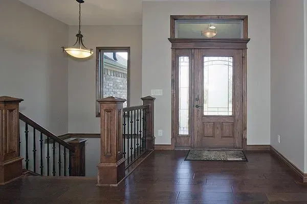 Empty foyer with dark wood floors, staircase, hanging light, and front door with sidelights.