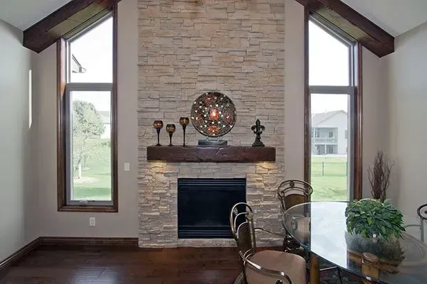 Living room with stone fireplace, tall windows, and glass dining table beneath a vaulted ceiling