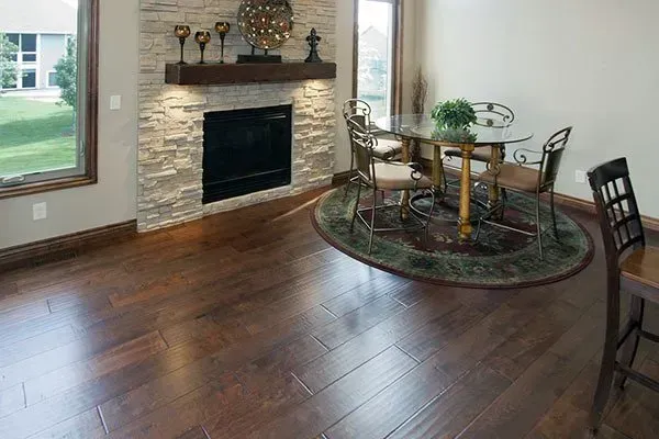 Living room with dark hardwood floors, stone fireplace, and round dining table by a window