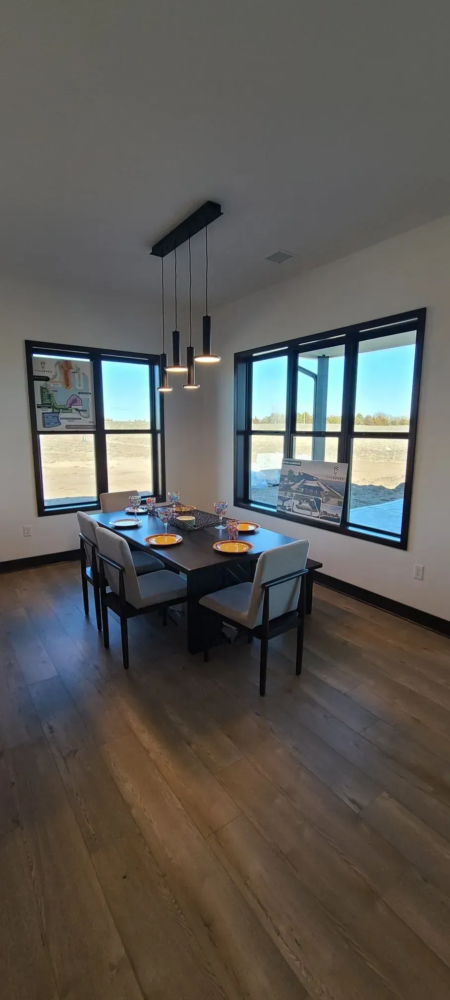 Modern dining room with black table, four chairs, large windows, and wood floors, with an open view outside