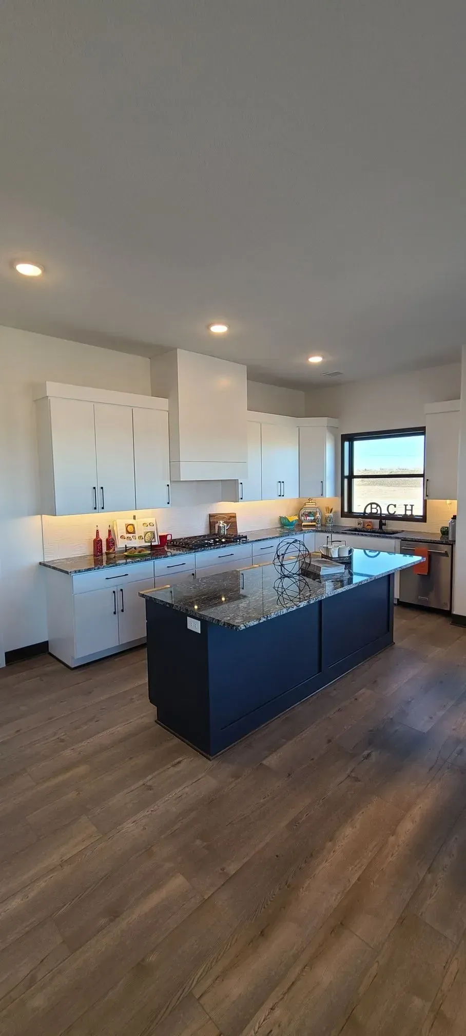 Modern kitchen with white cabinets, dark island, wood floors, and recessed lighting