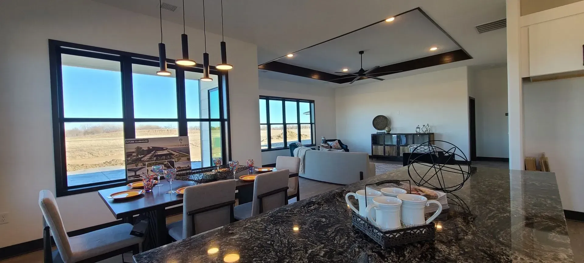 Open-plan kitchen and dining area with granite island, pendant lights, and large windows overlooking a landscape