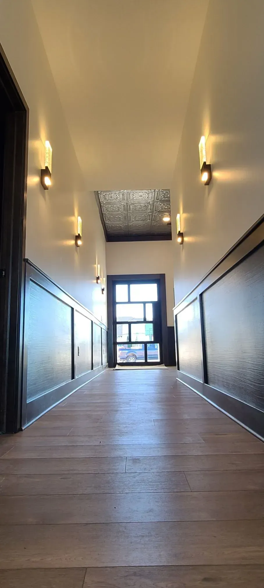 Narrow hallway with wood floors, dark walls, and a bright window at the far end