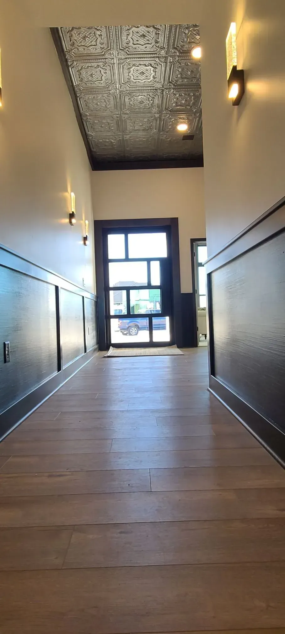 Empty hallway with wooden floors, black trim, and a bright glass door at the end
