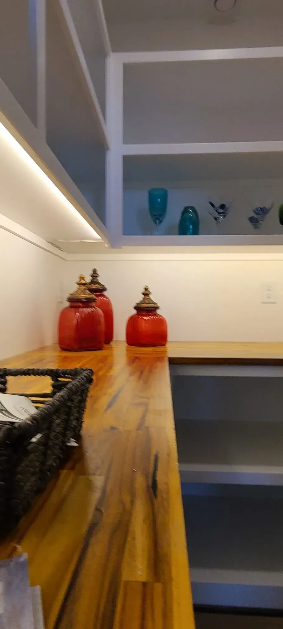 Kitchen shelf with two red jars on a wooden counter beneath open white shelving