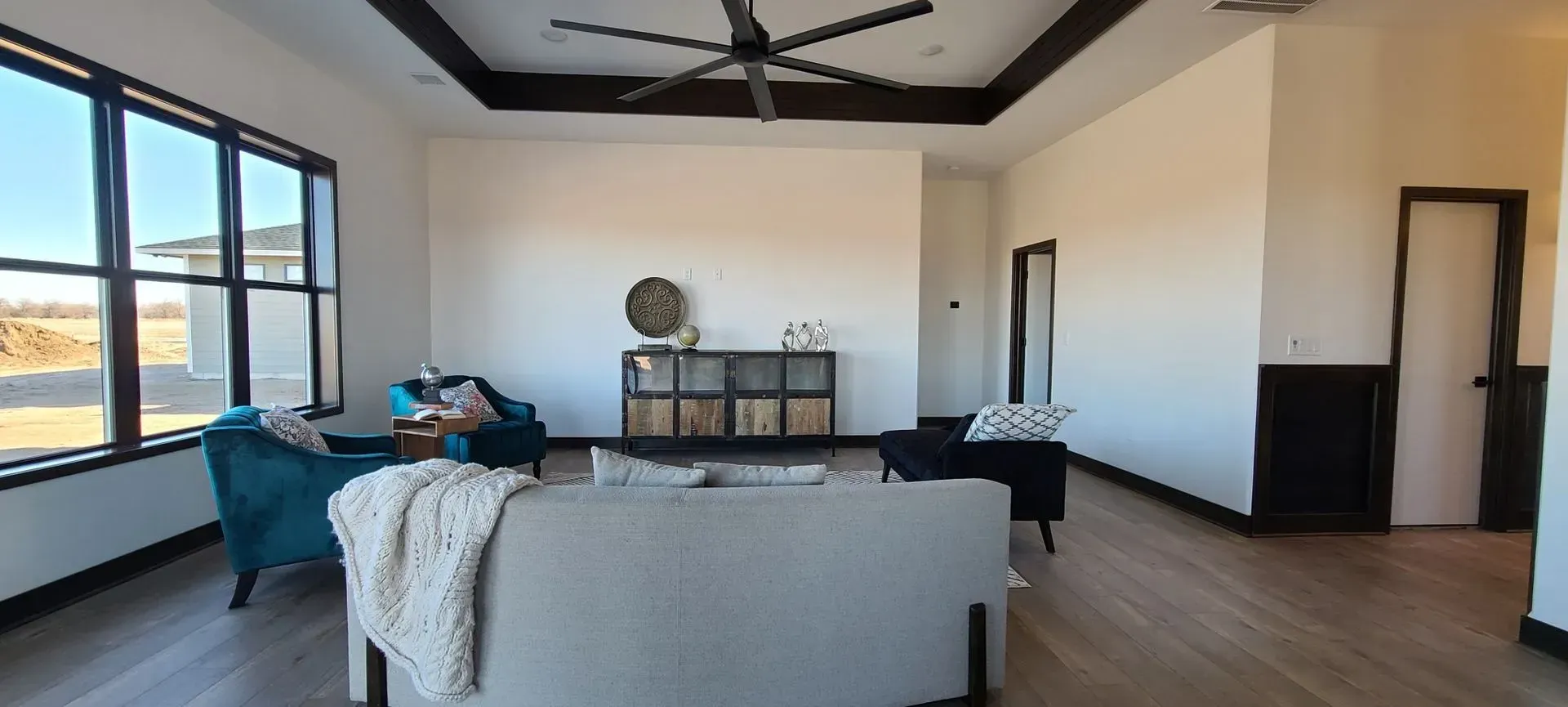 Bright modern living room with gray sofa, large windows, wood floor, and ceiling fan